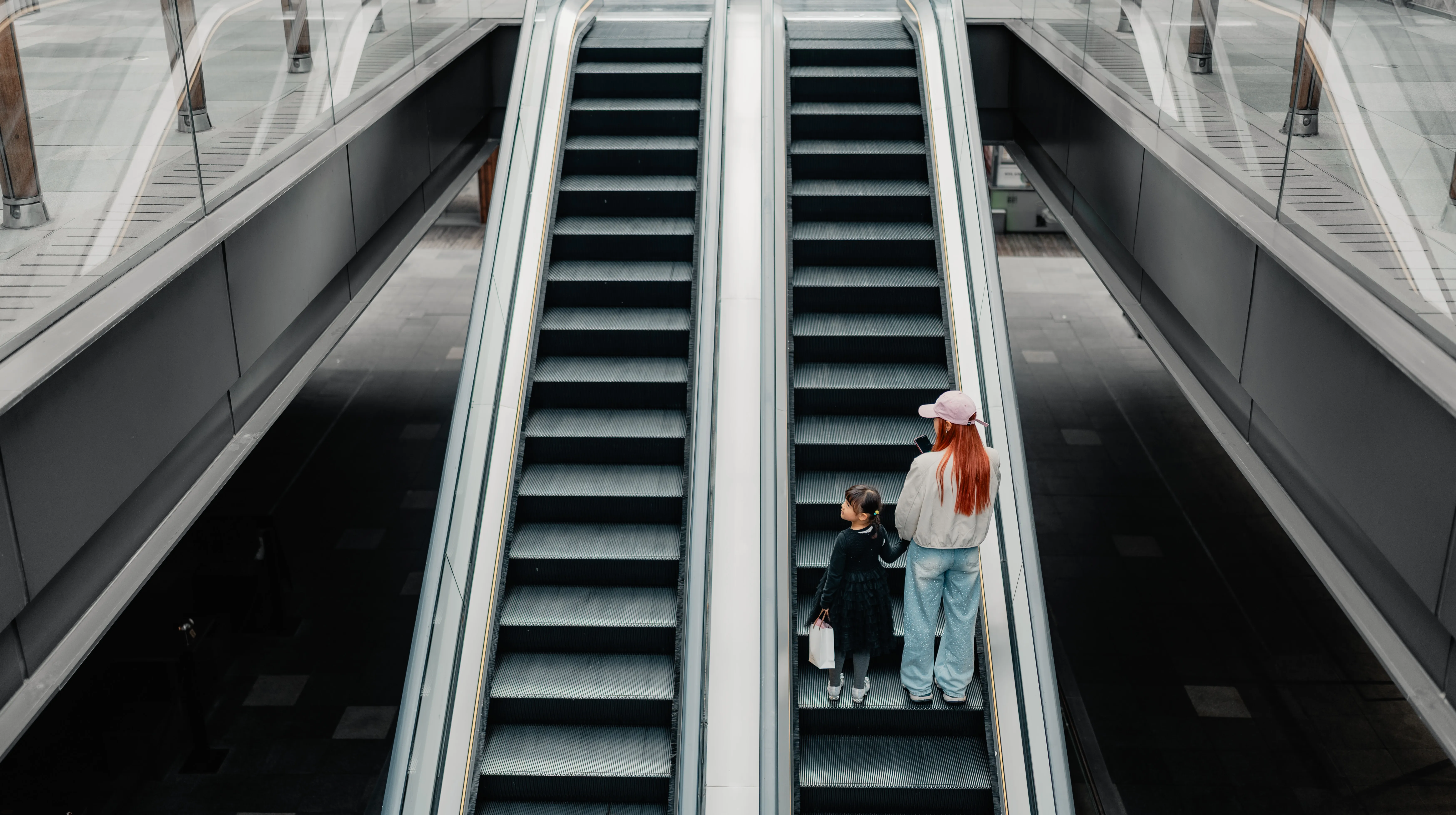 A mother and child riding an escalator down through a polished mall