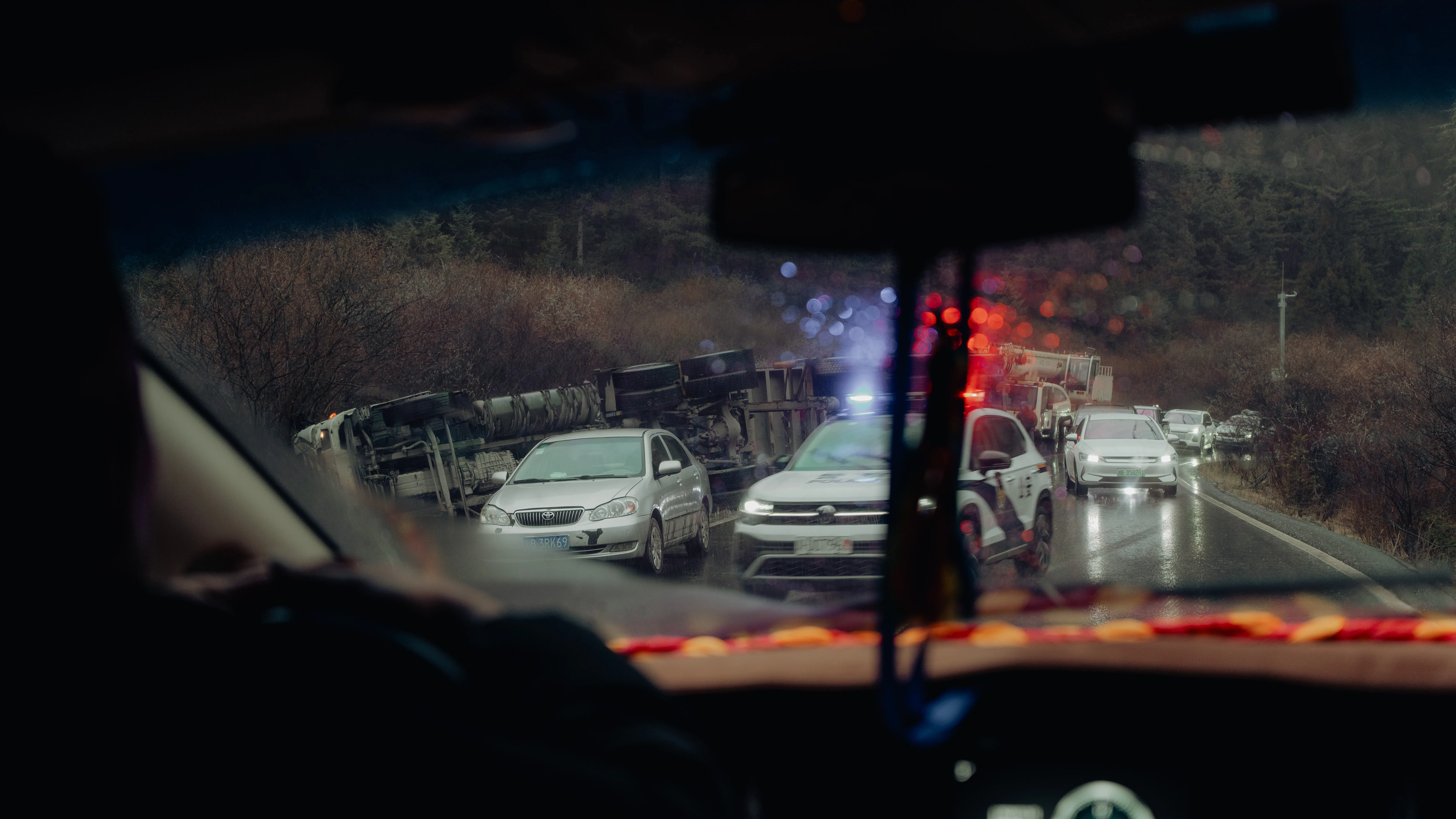 Traffic seen from the passenger seat at dusk, a truck tipped on the shoulder
